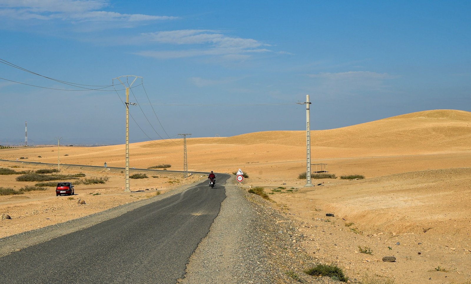 Motorcyclists and a car travelling on a remote paved road through Morocco desert hills